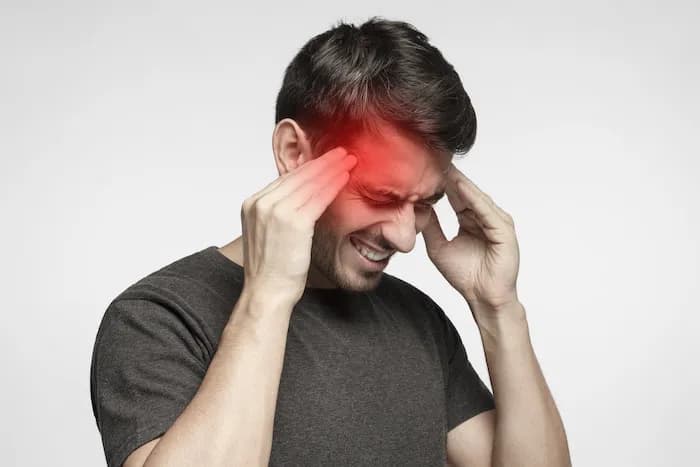 Homem com as mãos na cabeça, demonstrando dor de cabeça intensa.
